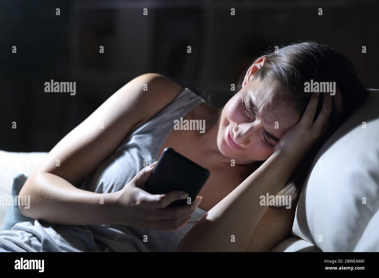 Triste femme se plaignant d'un smartphone assis dans le canapé la nuit à la maison Banque D'Images