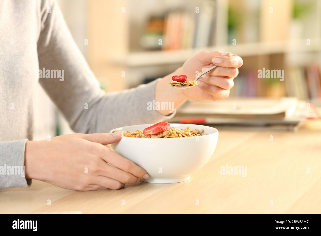 Gros plan des mains de femme en train de manger un bol à céréales assis sur une table à la maison Banque D'Images