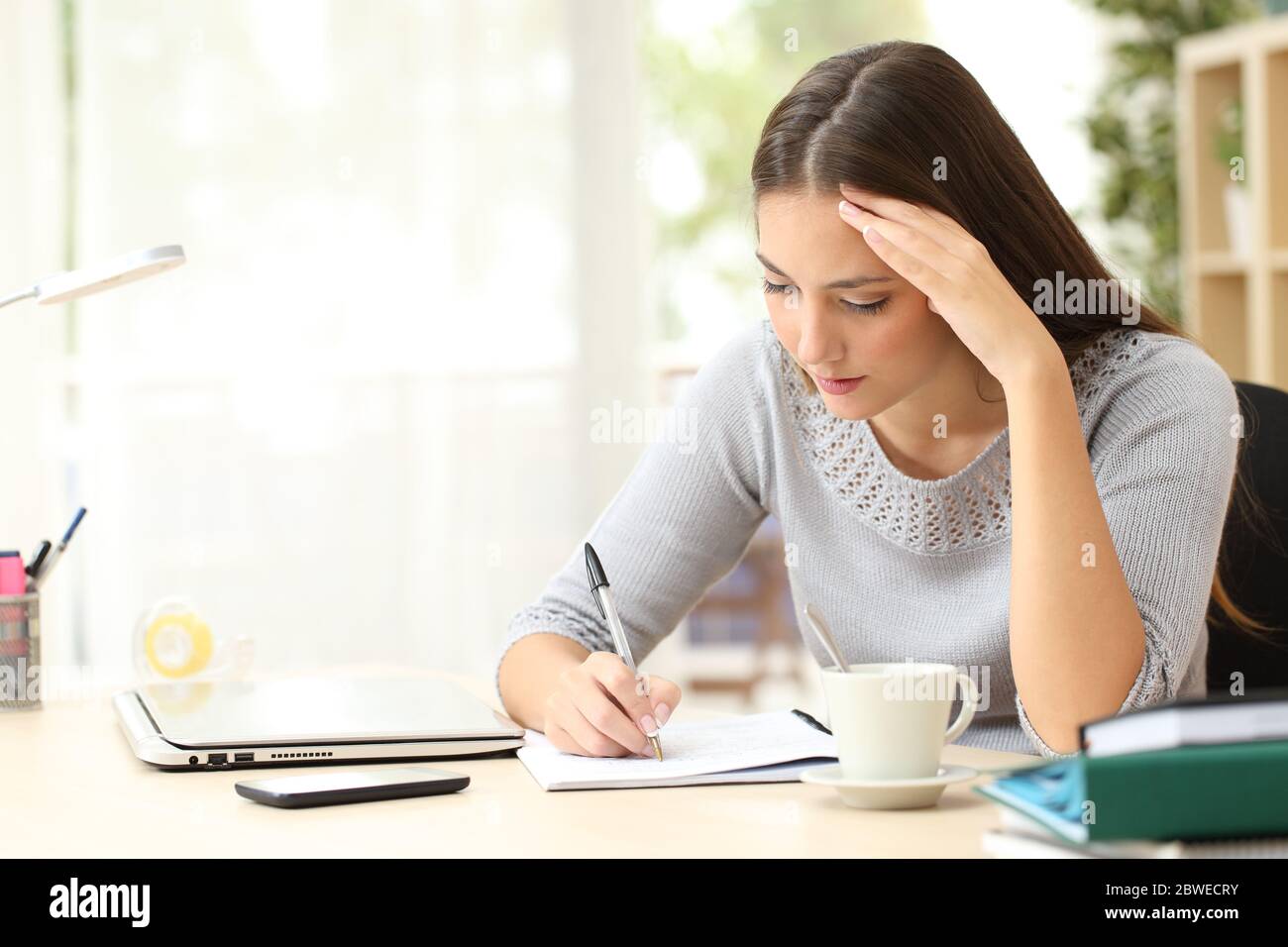 Femme concentrée écrivant des notes sur le carnet assis sur un bureau à la maison Banque D'Images