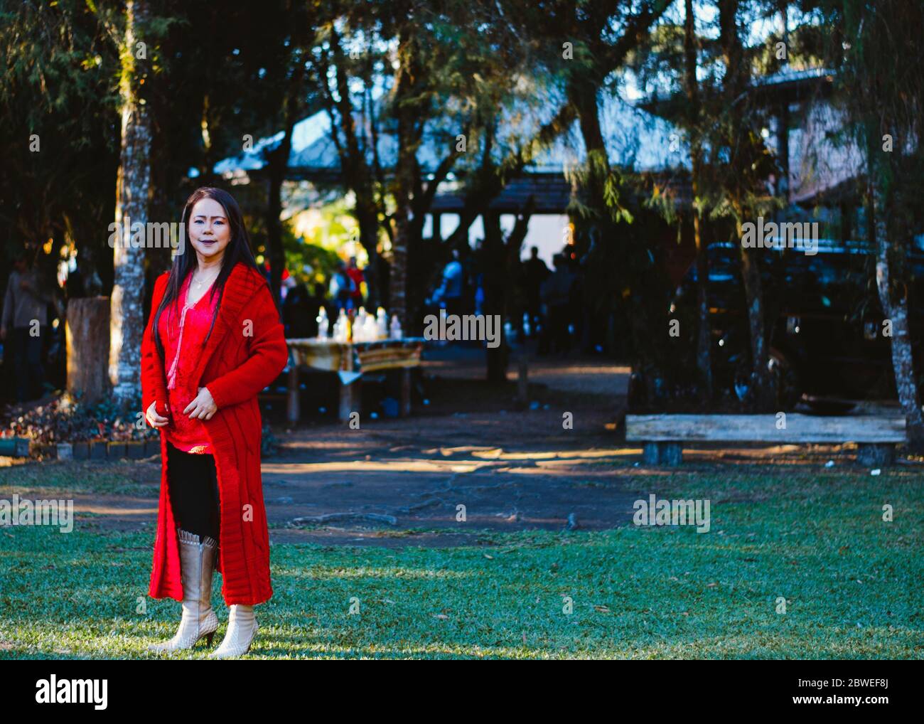 Une femme mature dans ses années 50 utilisant des vêtements élégants, des combinaisons rouges et des bottes en cuir beige posant devant une zone ouverte dans le parc. Banque D'Images