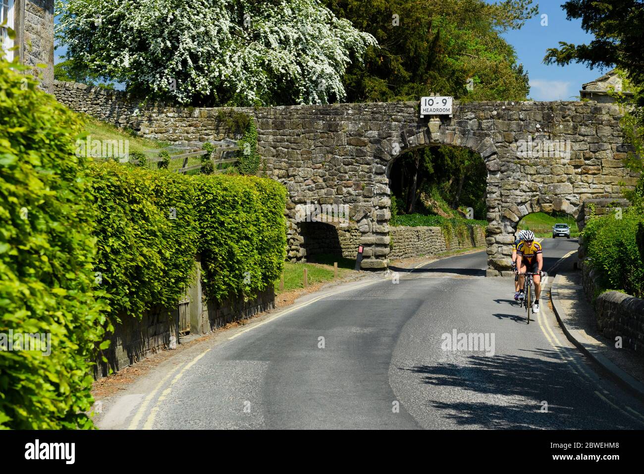 2 cyclistes sur la route de campagne en pierre (3 arches, panneau d'avertissement de hauteur 10' 9'') - B6160, village de Bolton Abbey, Yorkshire, Angleterre, Royaume-Uni. Banque D'Images