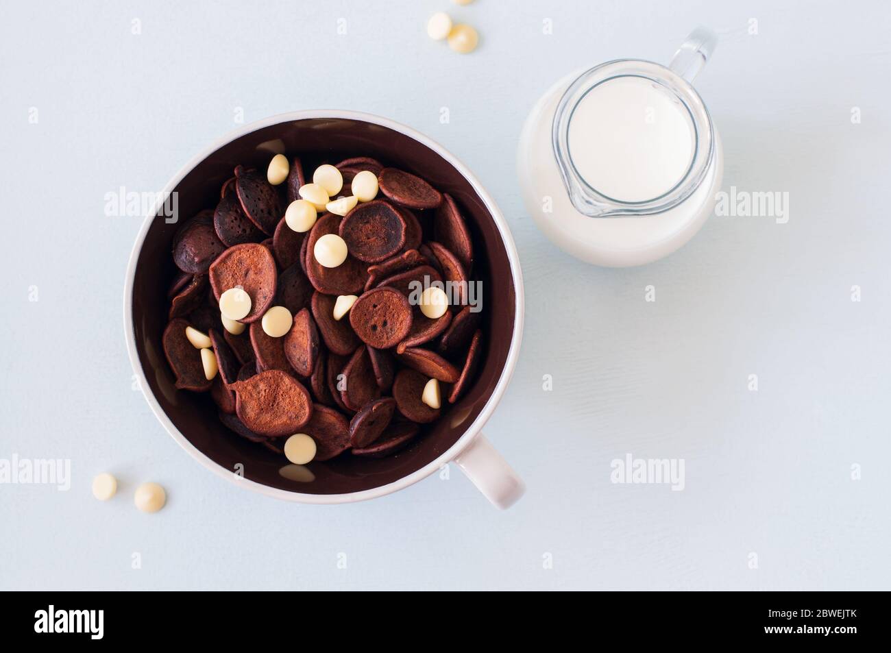 Chocolat de minuscules céréales pancakes avec du chocolat blanc dans un bol et du lait. Vue de dessus. Mettre en quarantaine les aliments tendance ou le nouveau concept normal. Banque D'Images