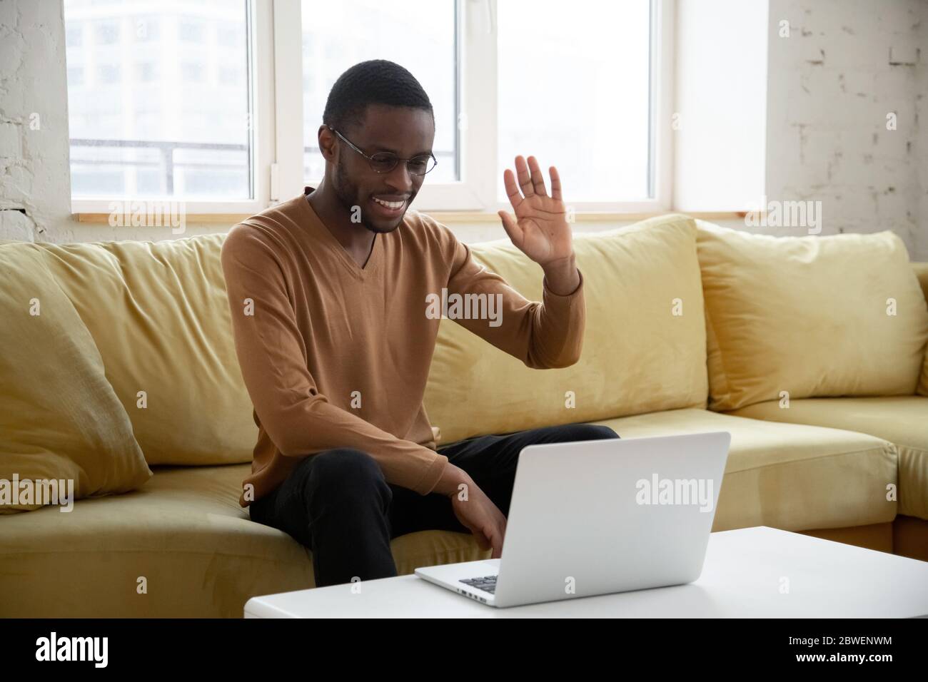 Un homme africain assis sur un canapé rend videocall saluant ami Banque D'Images