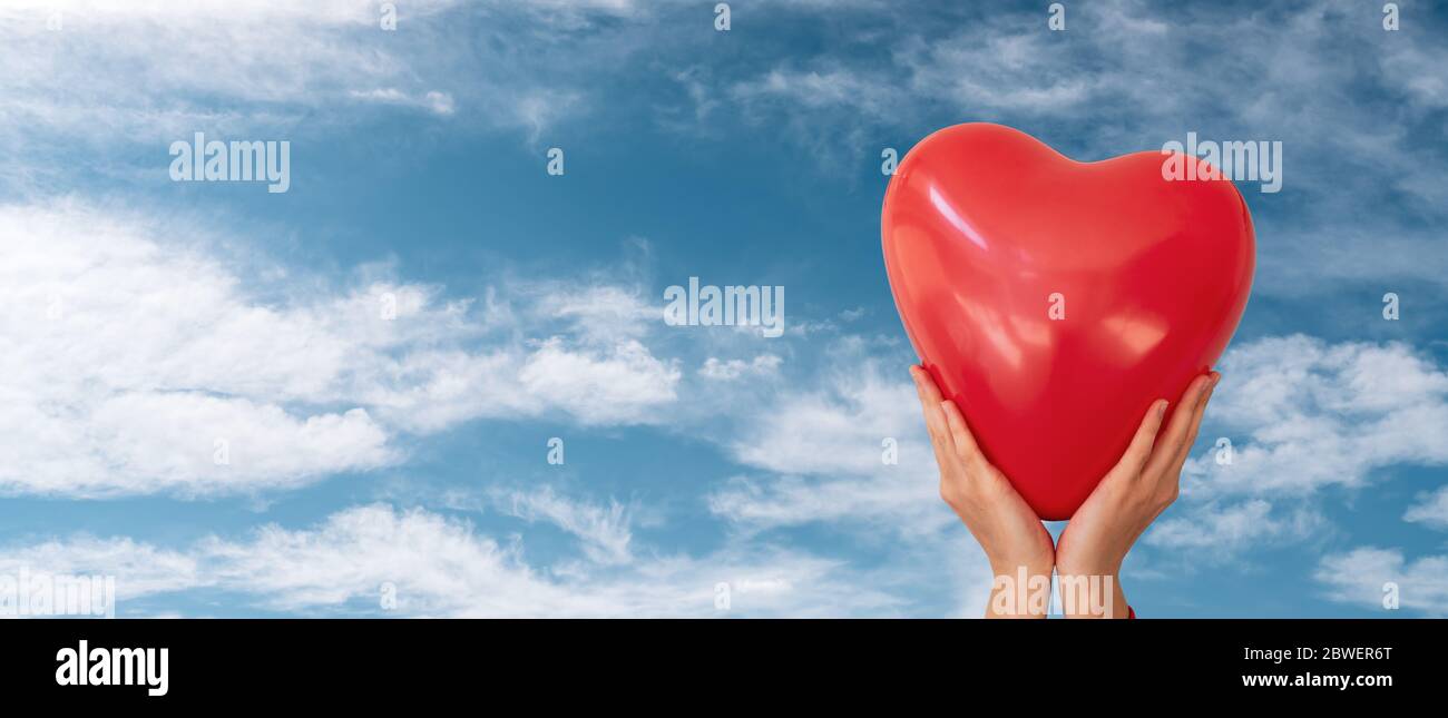La femme tient le ballon en forme de coeur rouge sur le fond bleu ciel nuageux. Concept Saint Valentin et romance Banque D'Images