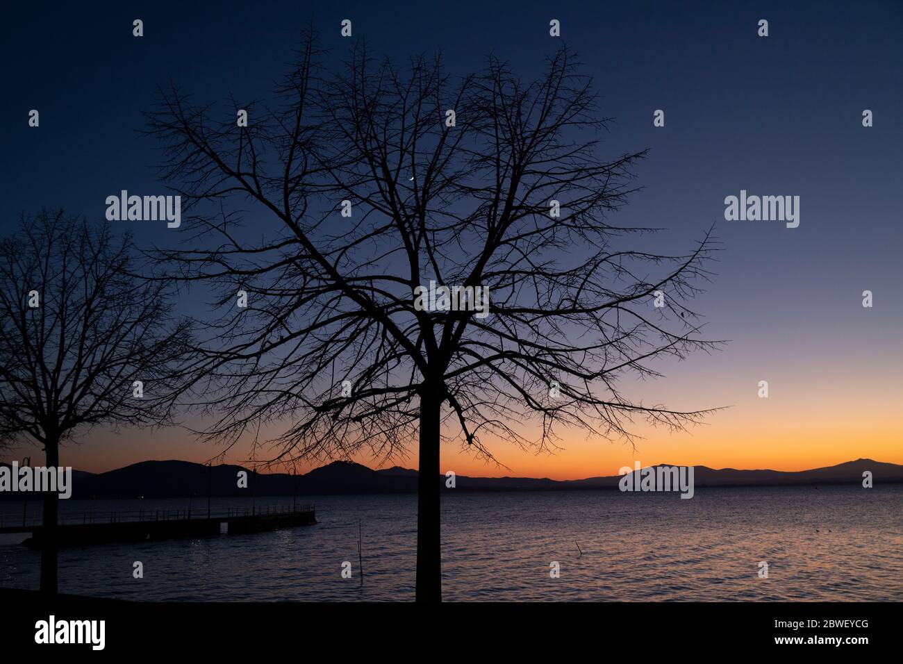 Coucher de soleil sur le lac Trasimène en Ombrie, Italie, avec des arbres contre la lumière Banque D'Images