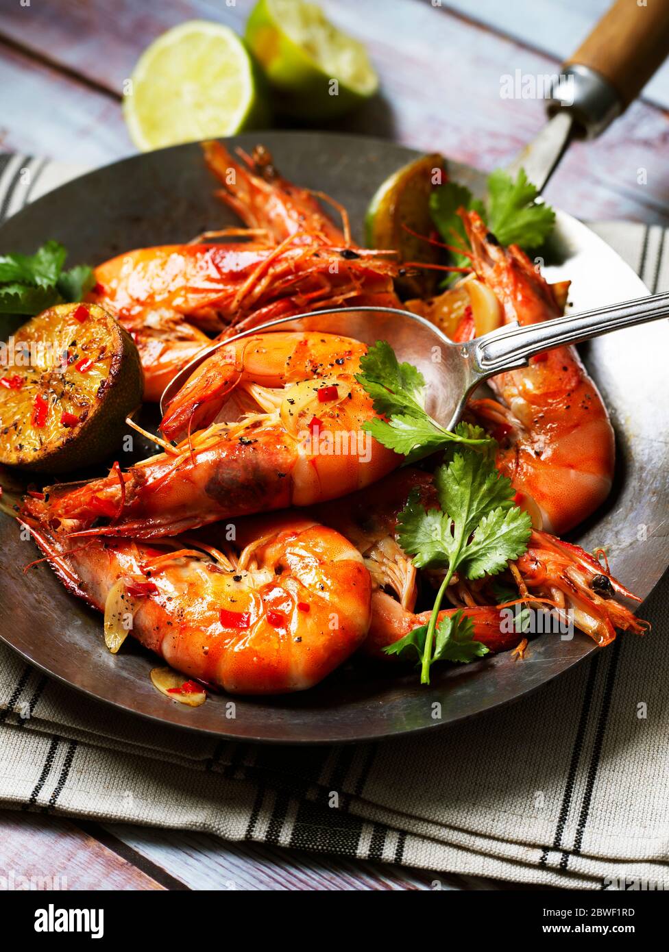 Décorez les crevettes dans une poêle avec du Chili, de l'ail, de la coriandre et de la lime sur une table en bois et une serviette de table Banque D'Images