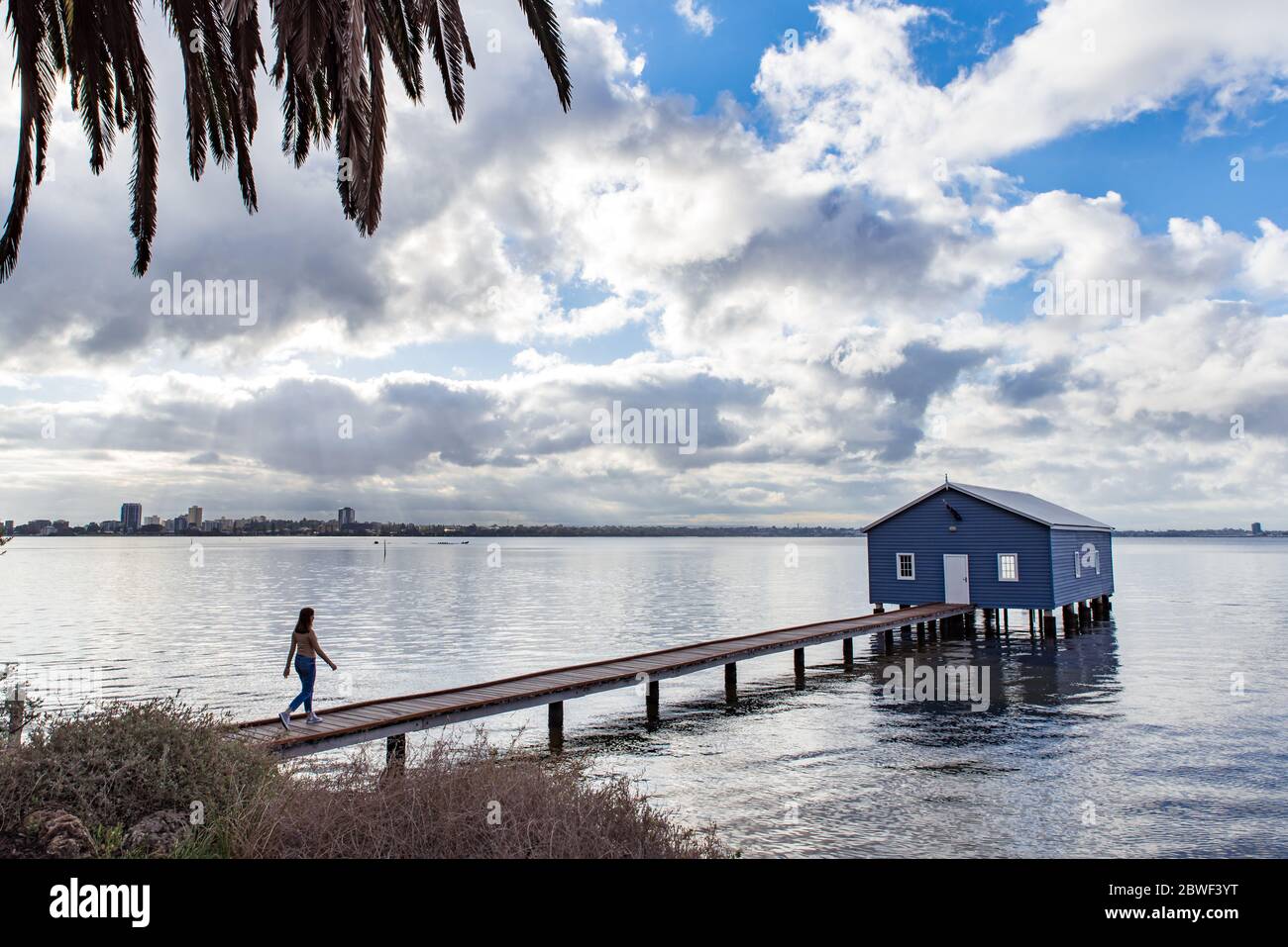 Perth, novembre 2019: Une fille touriste marchant sur la jetée, regardant la célèbre petite maison de bateau bleu - le Crawley Edge Boatshed situé sur la Swan River Banque D'Images