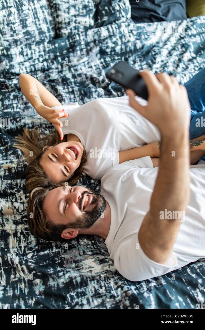 Vue de dessus de beau jeune couple aimant allongé dans le lit et faisant le selfie Banque D'Images