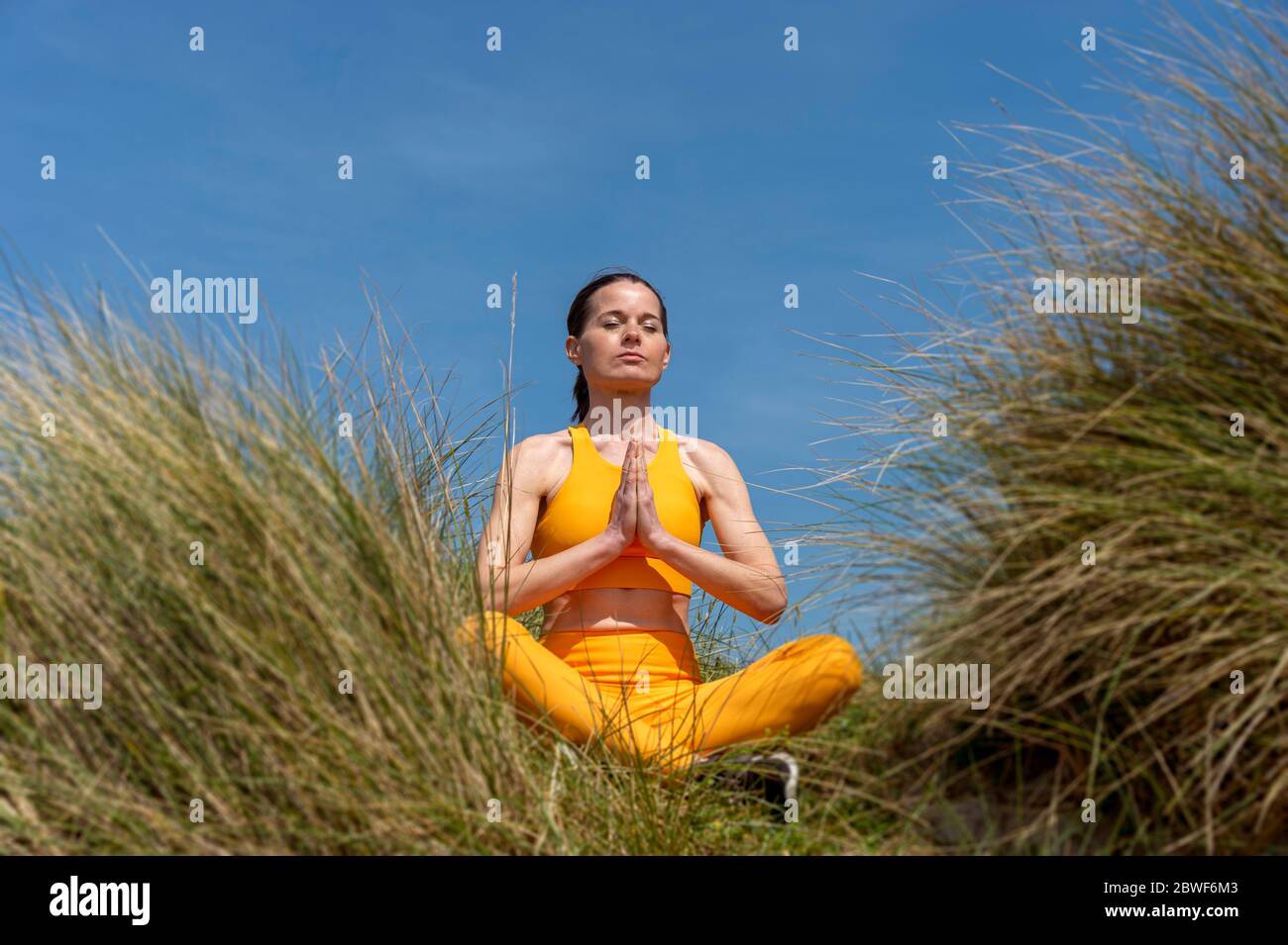 Femme pratiquant le yoga et méditant dans les dunes de plage avec le ciel bleu Banque D'Images