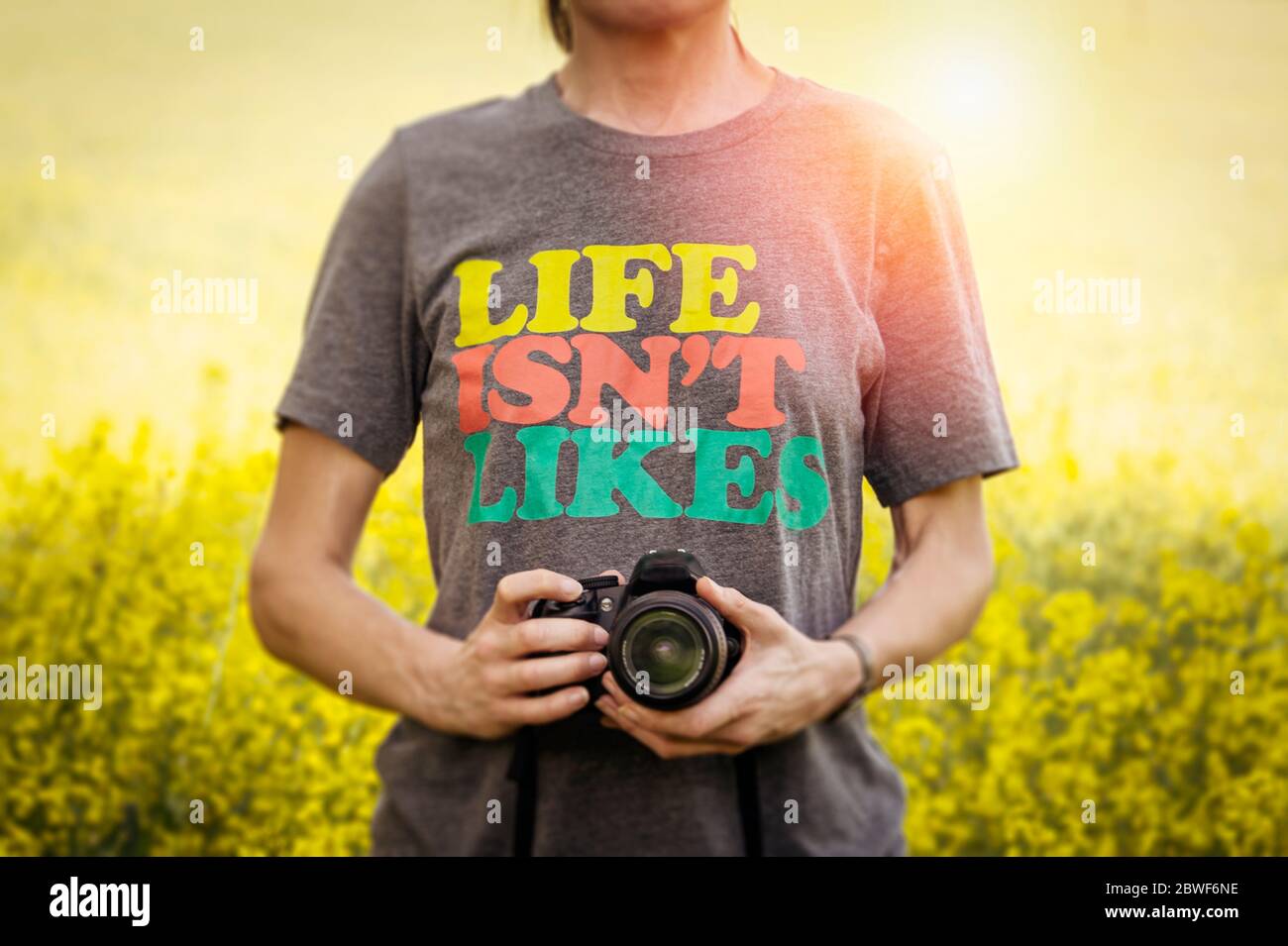 Femme tenant un appareil photo reflex numérique portant un t-shirt avec un t-shirt « la vie n'aime pas ». Banque D'Images