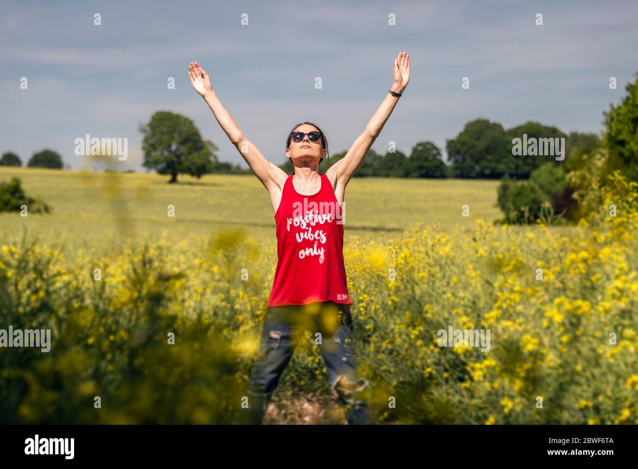 Jeune femme tenant les mains en haut tout en appréciant la chaude journée ensoleillée, positive vibes seulement débardeur. Banque D'Images