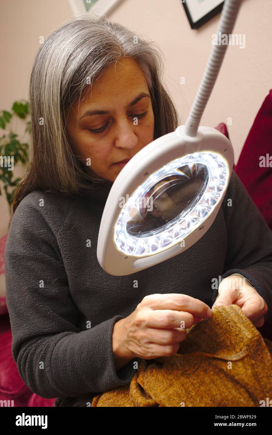 Femme qui coudre à l'aide d'une loupe éclairée pour aider à la finition des travaux. Banque D'Images