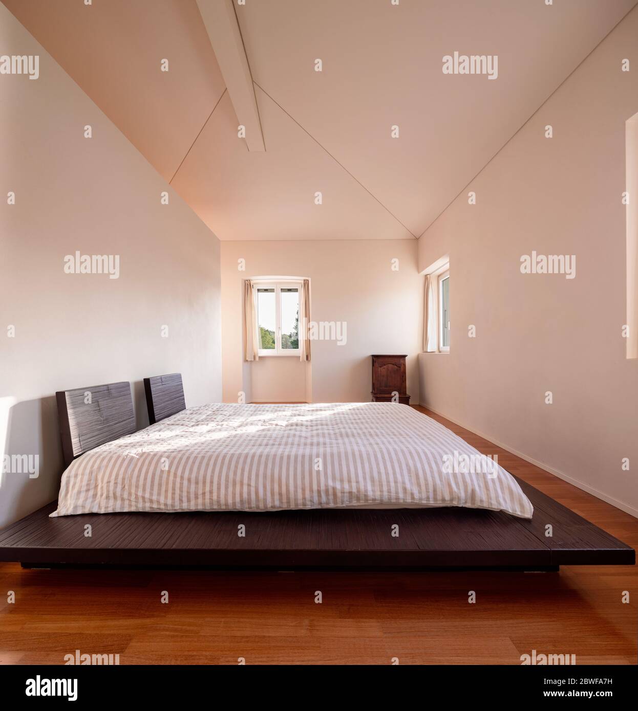 Intérieur d'une chambre minimale, avec un seul lit et un faisceau de lumière entrant. Le sol est en bois et le lit est bas, de style japonais. Banque D'Images