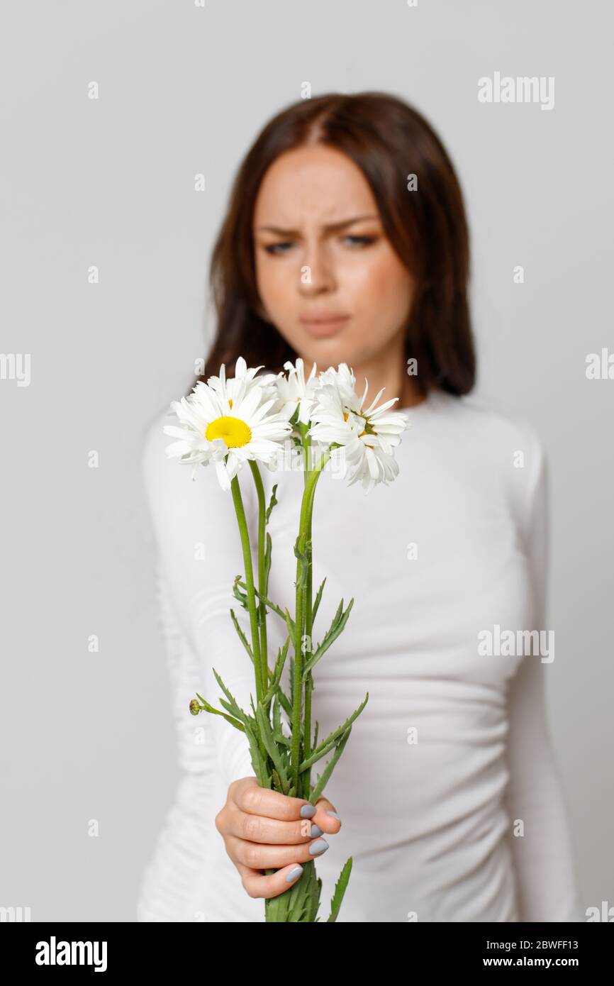 Studio portrait de la femelle allergique brunette en blanc haut tenant un bouquet de fleurs, ayant une réaction allergique à la camomille, foyer sélectif.aller Banque D'Images