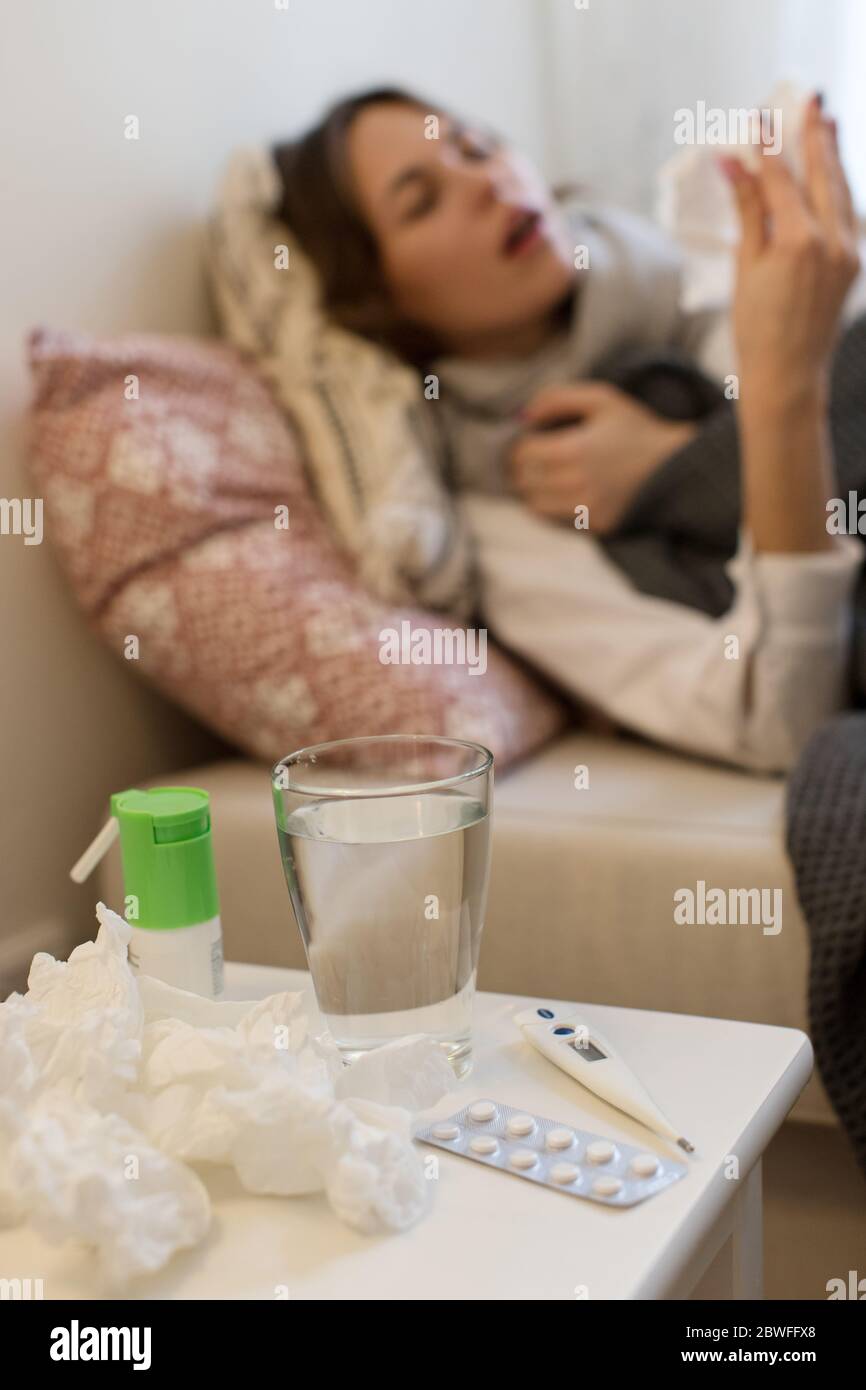 Malade flou jeune femme caucasienne allongé sur un canapé, enveloppée dans un foulard, sous la housse, ayant des symptômes de grippe, éternuant dans un mouchoir, se concentrer sur le TH Banque D'Images