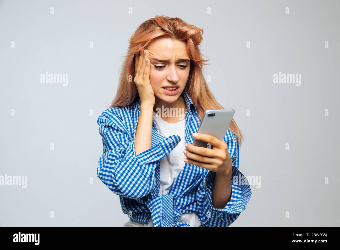 Choqué surpris jeune femme mignonne avec des cheveux blonds de fraise  regardant son téléphone, reçoit des sms, des nouvelles, message, touchant  son front, isolé sur g Photo Stock - Alamy