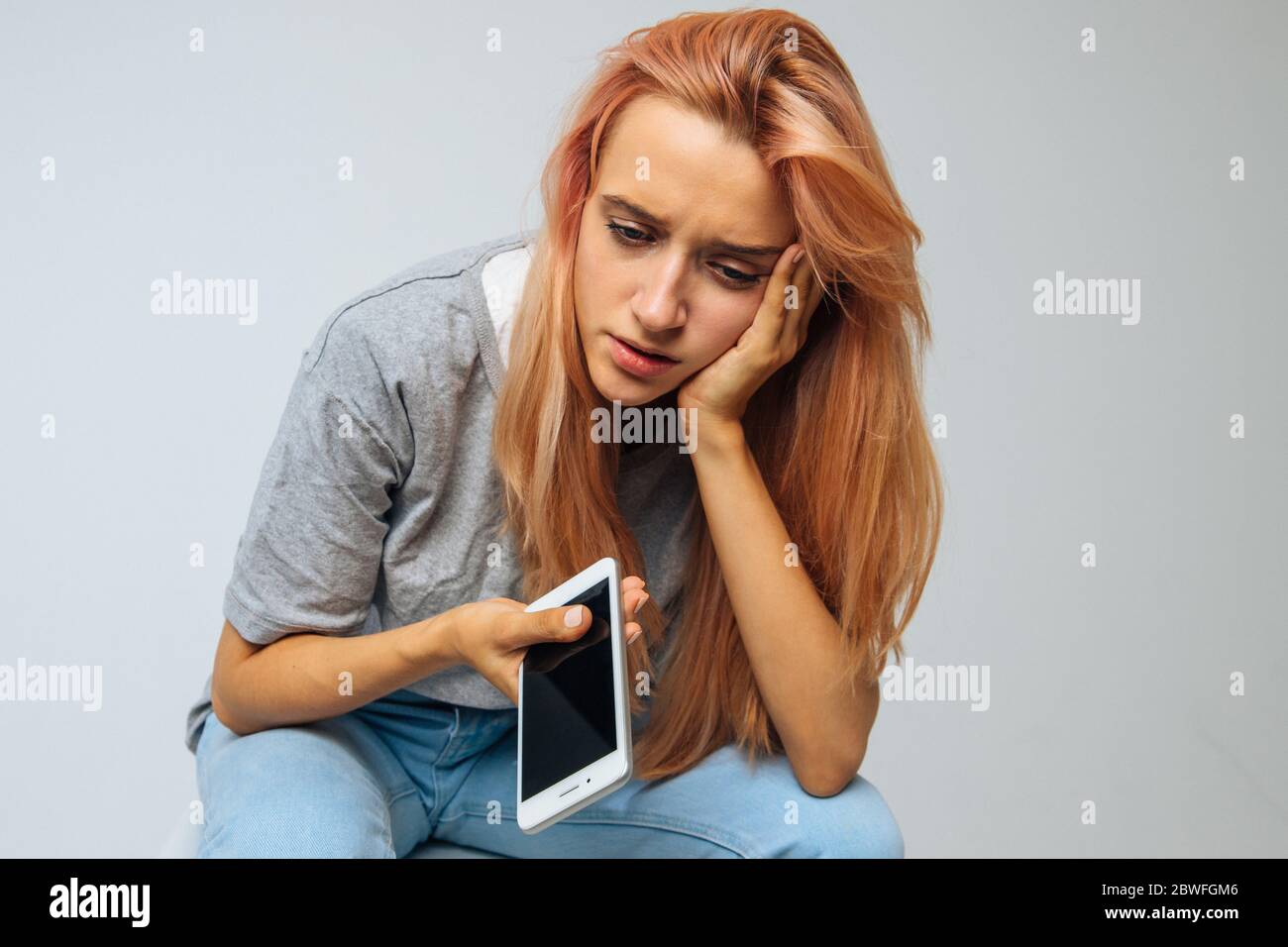 Pleurer une jeune femme solitaire en dépression regardant vers le bas, tenant un smartphone, obtient de mauvaises nouvelles et se touchant la tête. Problème dans les relations, la relation Banque D'Images