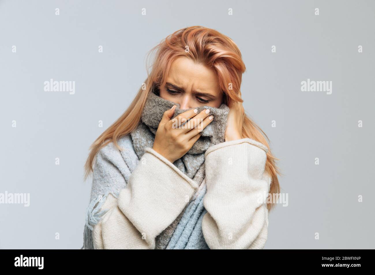 Bouleversé jeune femme caucasienne avec des cheveux blonds de fraise enveloppés dans un foulard chaud, se sent mal, regardant vers le bas, gros plan.malade désespéré femme a la grippe. Rh Banque D'Images