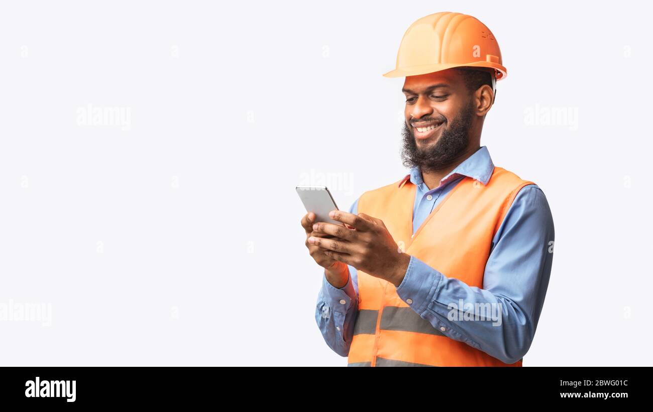 Travailleur de l'African Builder utilisant un smartphone sur fond de White Studio, Panorama Banque D'Images