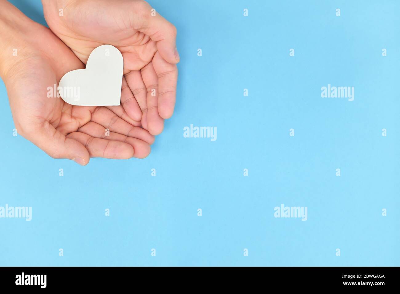Mains en forme de cuppée tenant un cœur blanc sur fond bleu. Charité, amour pur, compassion et bonté concept. Vue de dessus. Banque D'Images