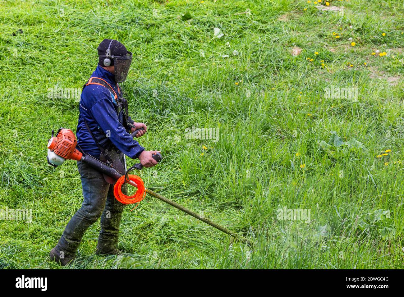 tondeuse homme avec tondeuse à ficelle et masque de visage trimmong herbe - gros plan Banque D'Images