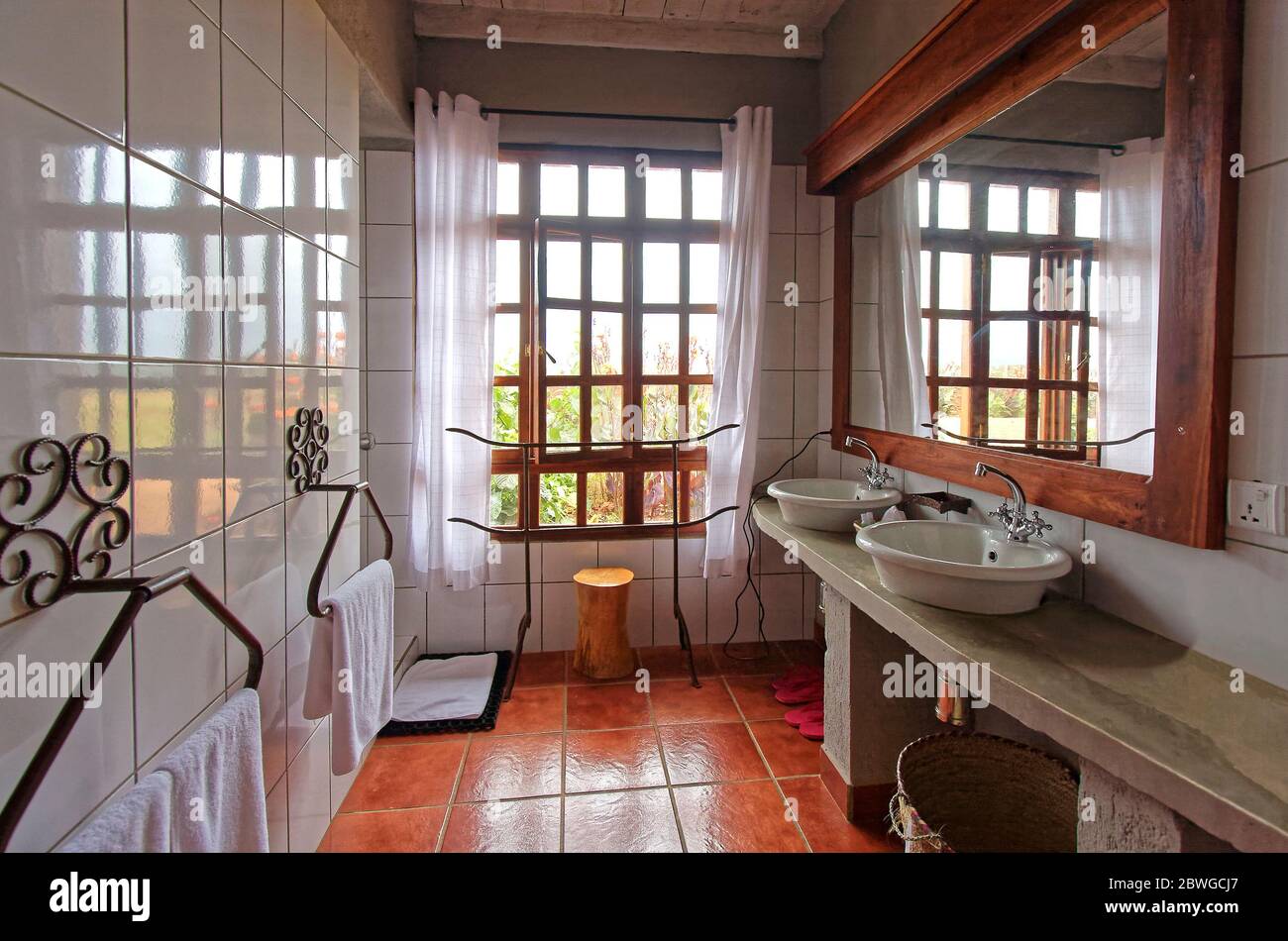 Salle de bains moderne, double vasque lavabos, sol en carreaux de rouille, porte-serviettes richement ornés, grande fenêtre, miroir, Ngorongoro Farmhouse Valley Lodge; Tanzanie, Afrique Banque D'Images