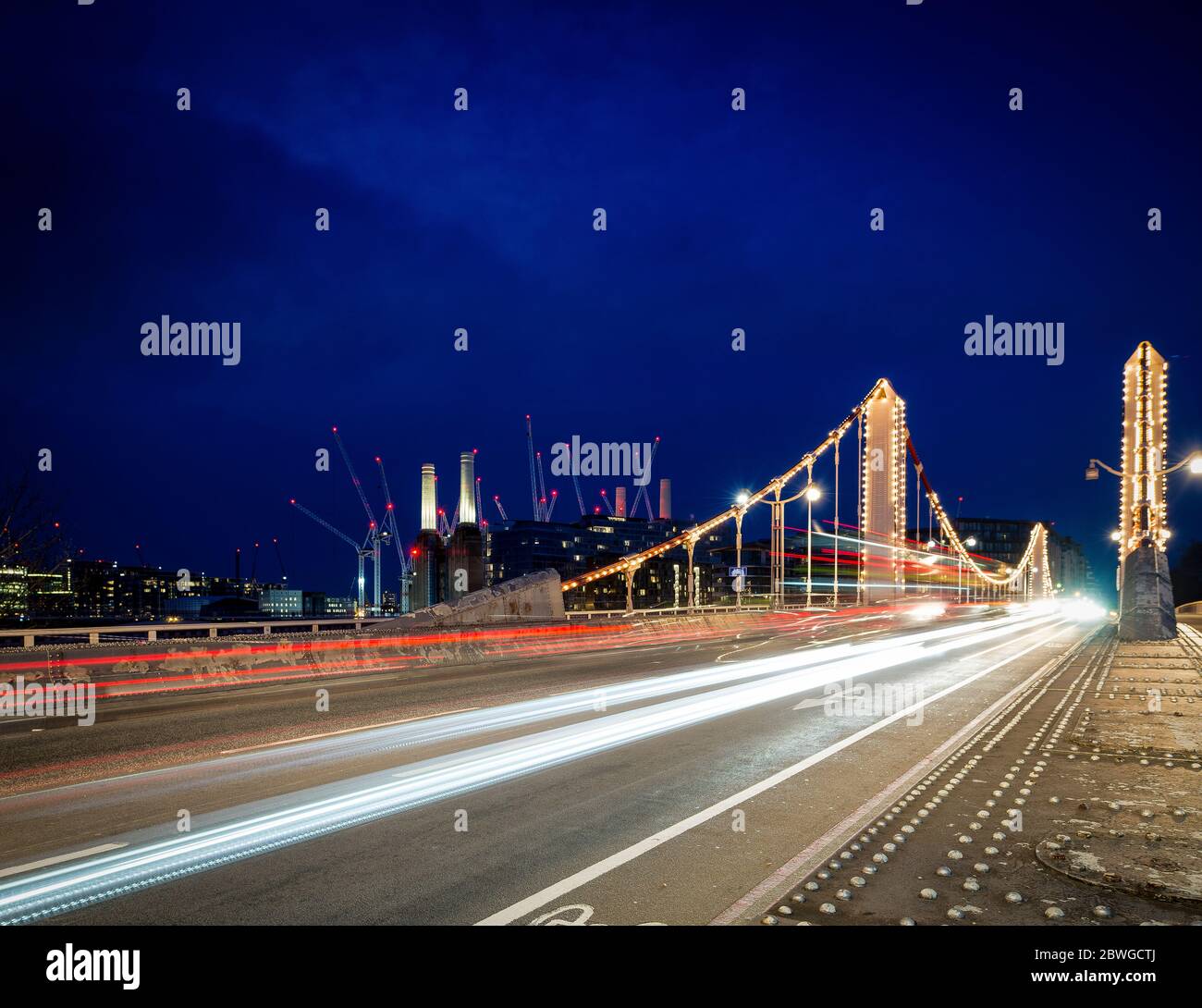 Albert Bridge illuminé la nuit avec des traînées de lumière provenant de la circulation de passage et Battersea Power Station en arrière-plan, Londres, Royaume-Uni. Banque D'Images