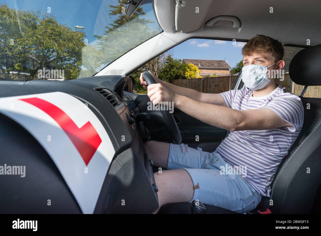 L'adolescent conducteur a portant un masque facial en raison de la pandémie du coronavirus attendant de commencer sa leçon de conduite. Banque D'Images