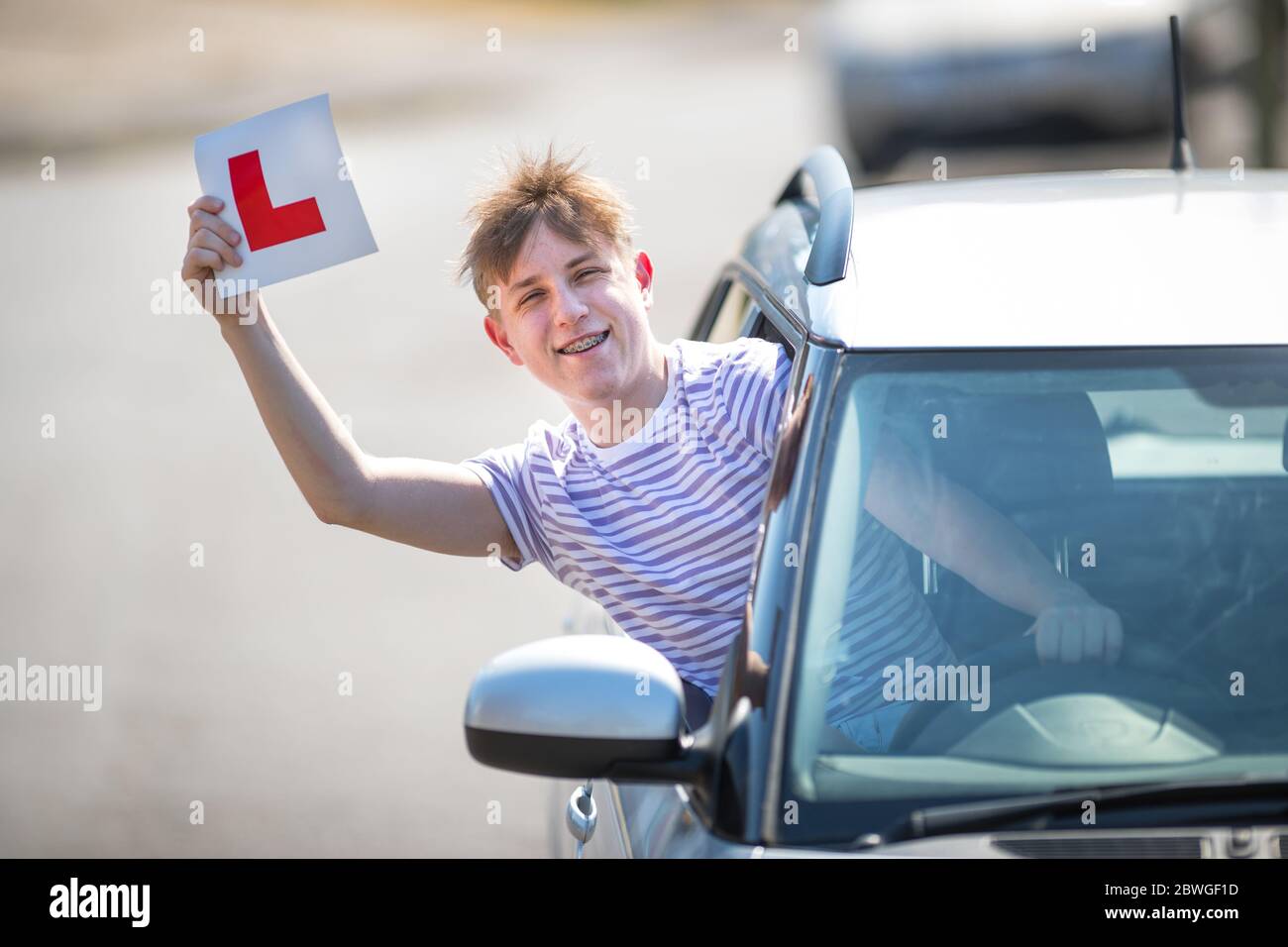Un jeune conducteur apprenant qui célèbre son passage à l'essai routier en agitant ses plaques en L dans l'air. Banque D'Images