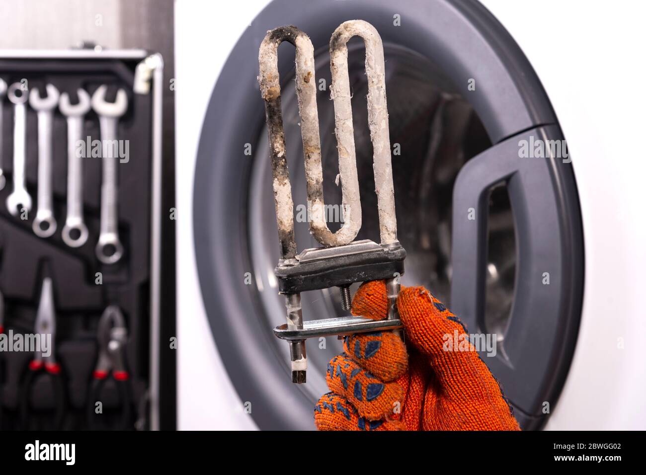 Réparation de machines à laver. Main d'un réparateur avec un chauffage électrique turbulent recouvert d'un revêtement d'eau dure. Remplacement du chauffage électrique Banque D'Images