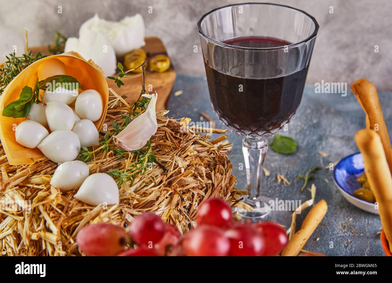 Fromage mozzarella sur un foin à l'ail et au raisin, un verre de vin rouge sur fond bleu. Banque D'Images