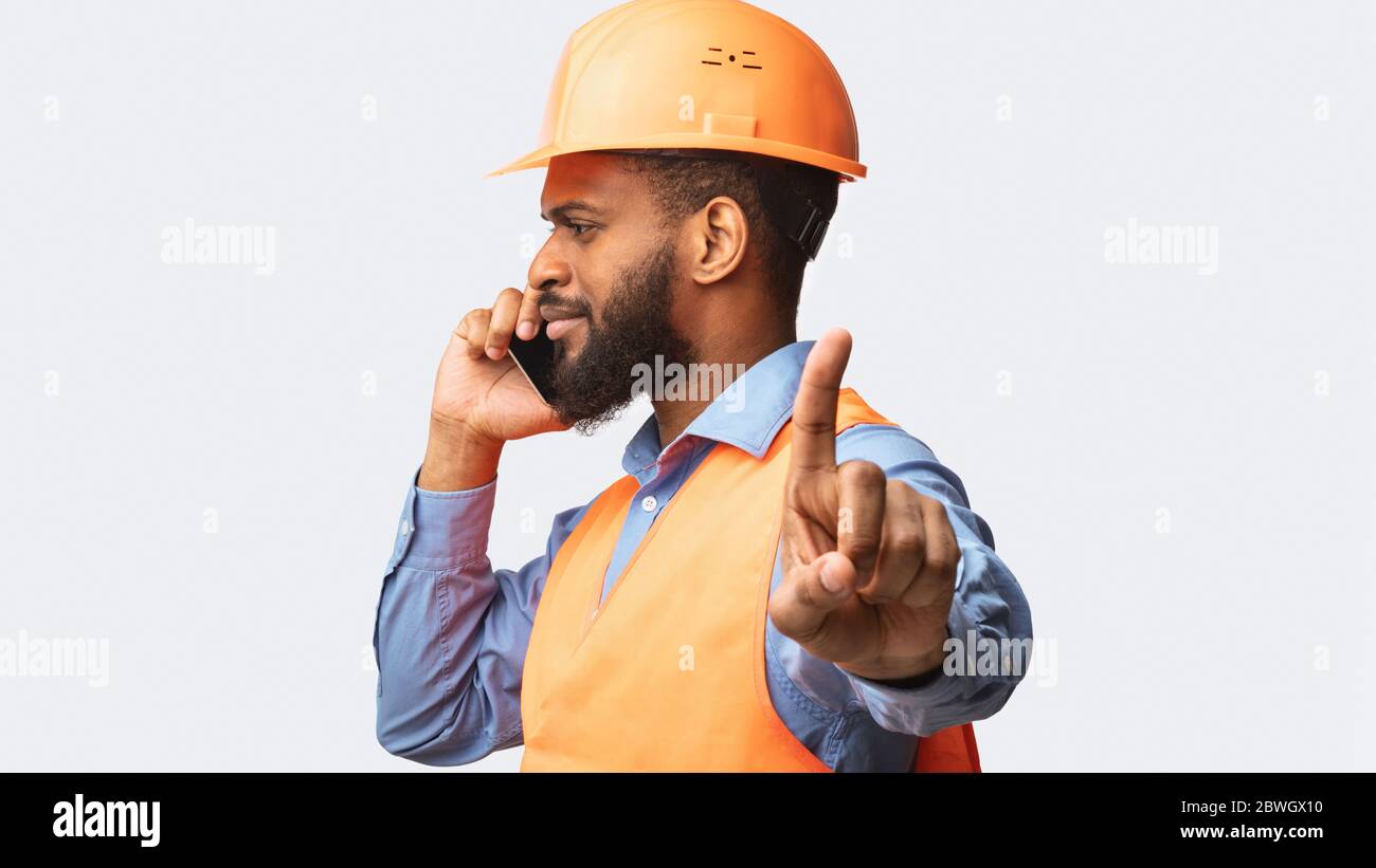 Travailleur de la construction parlant sur un téléphone portable en train de faire un geste d'attente, fond blanc Banque D'Images