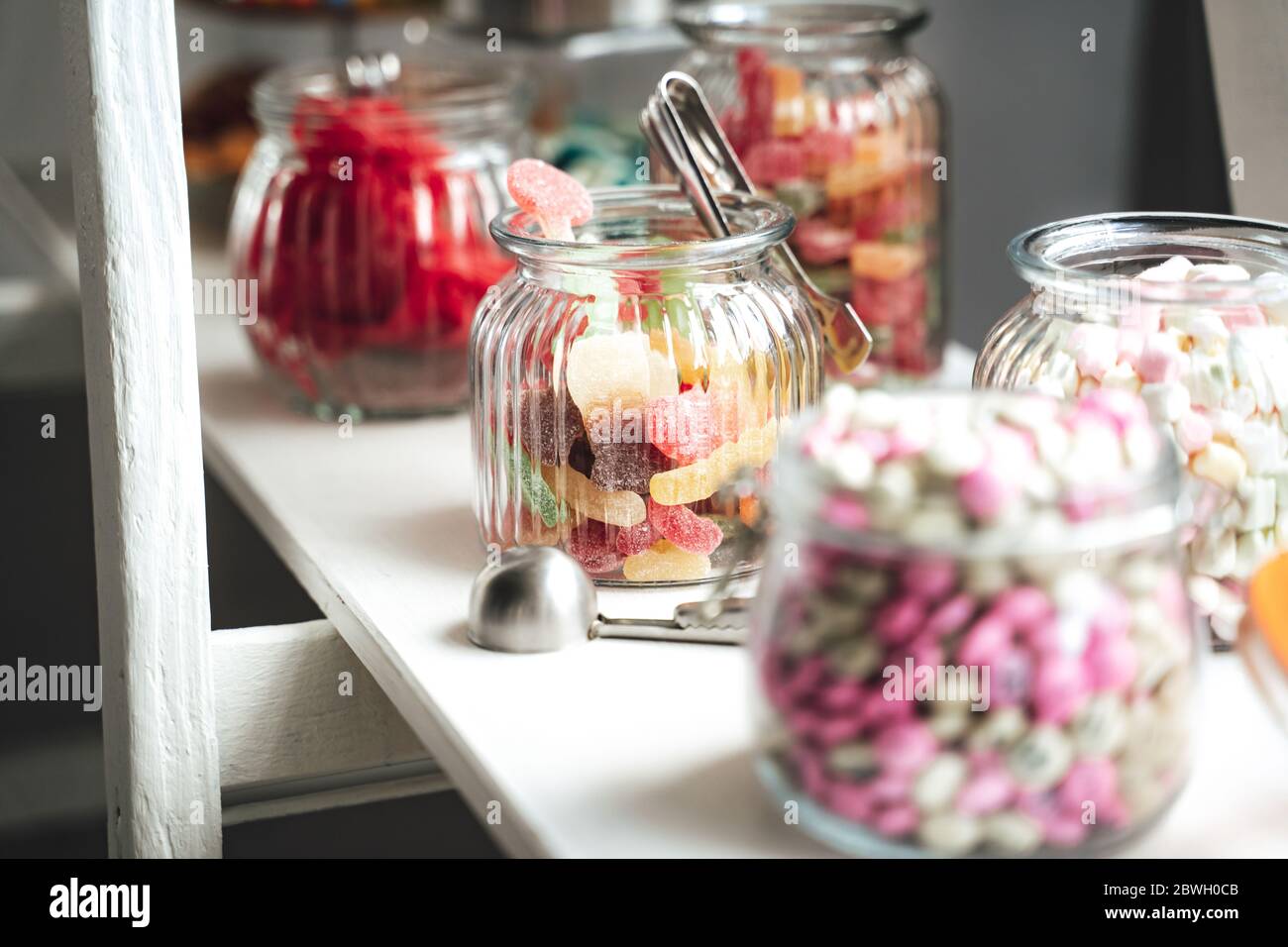 Barre de bonbons de plusieurs sortes de bonbons colorés dans des pots en verre sur étagère blanche. Concept mariage ou fête. Banque D'Images