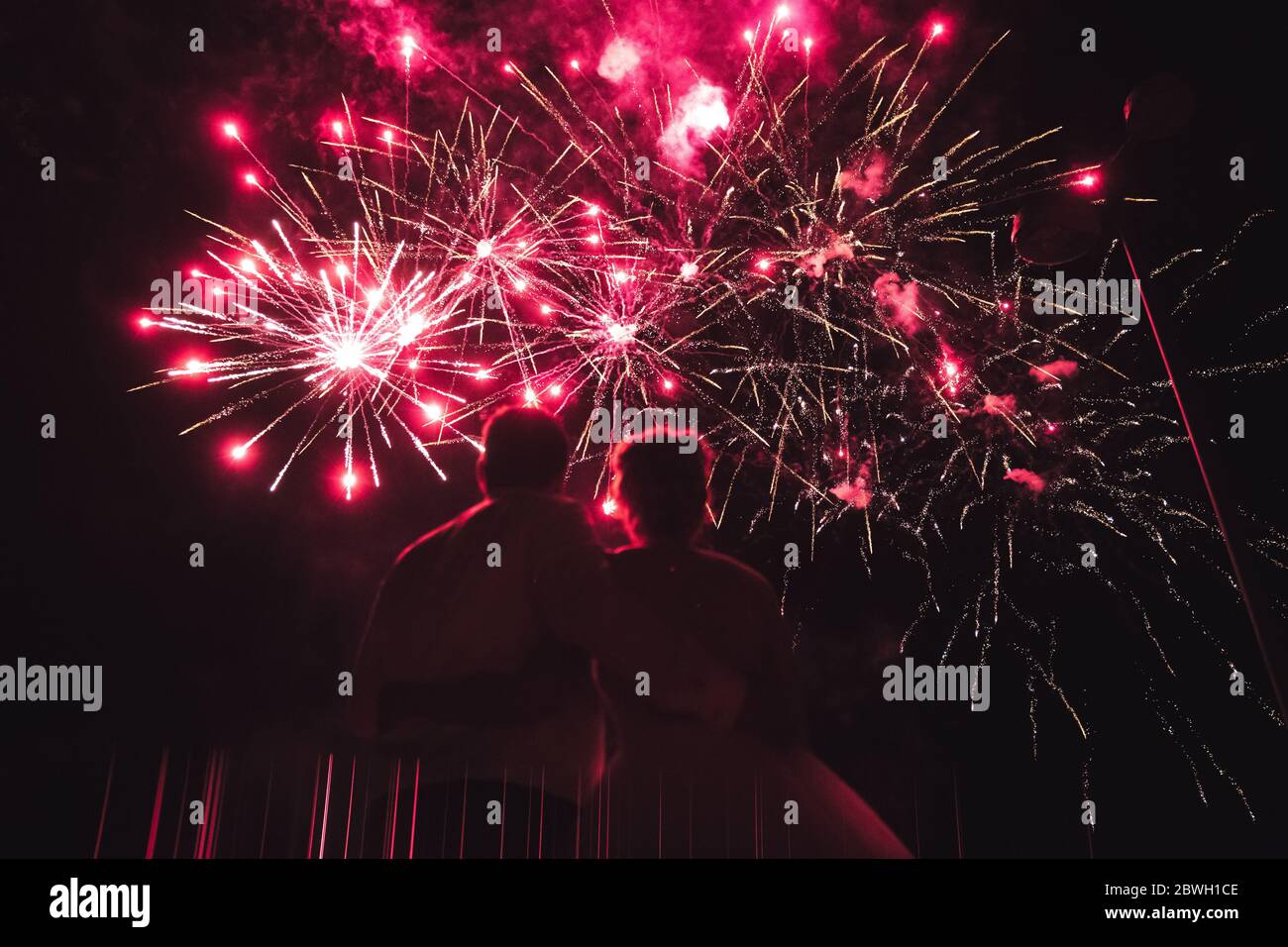 Vue arrière d'un couple qui regarde des feux d'artifice aux tons rouges. Deux paires de fêtes. Banque D'Images