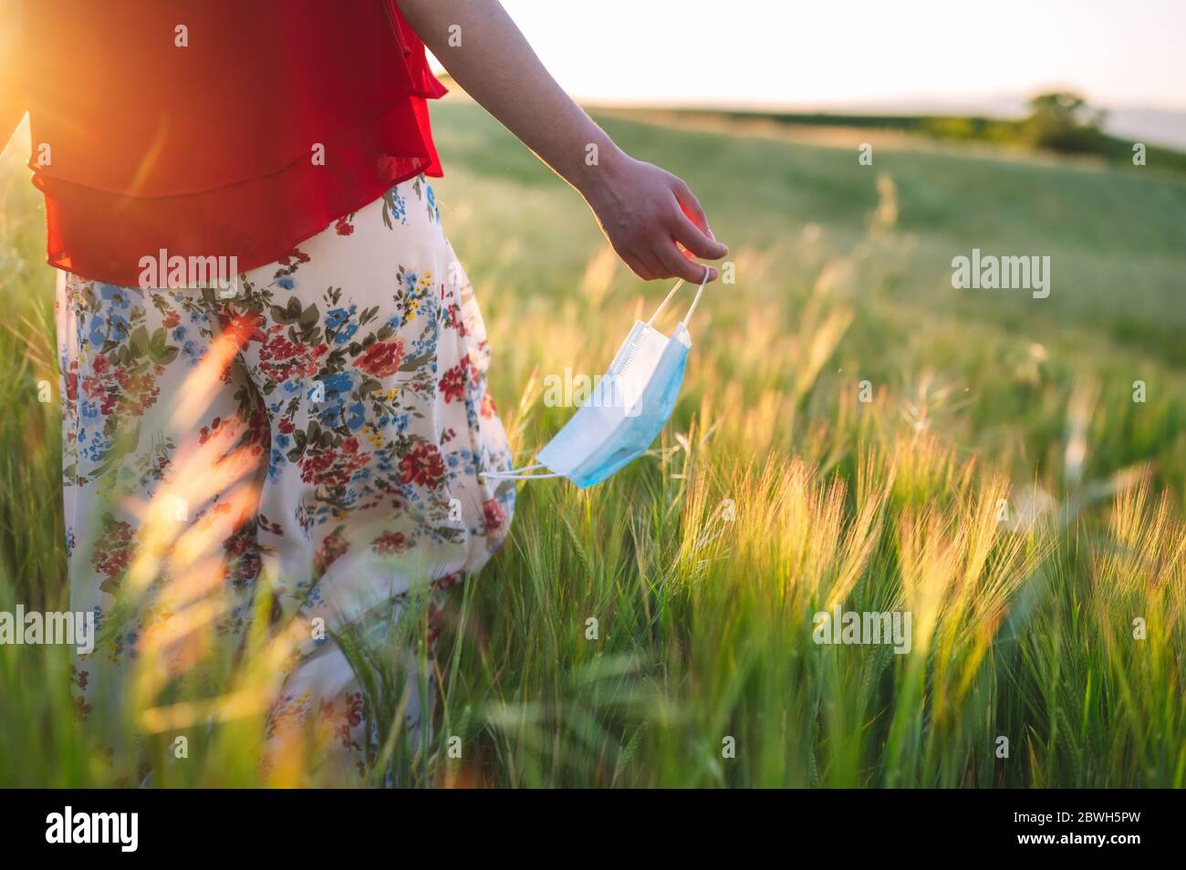 Gros plan sur une femme qui marche à l'extérieur en jetant son masque. Jeune fille heureuse enlever le masque de protection. Fin du concept de coronavirus pandémique. Paysage de prairie, allergie de pollen au printemps . Banque D'Images