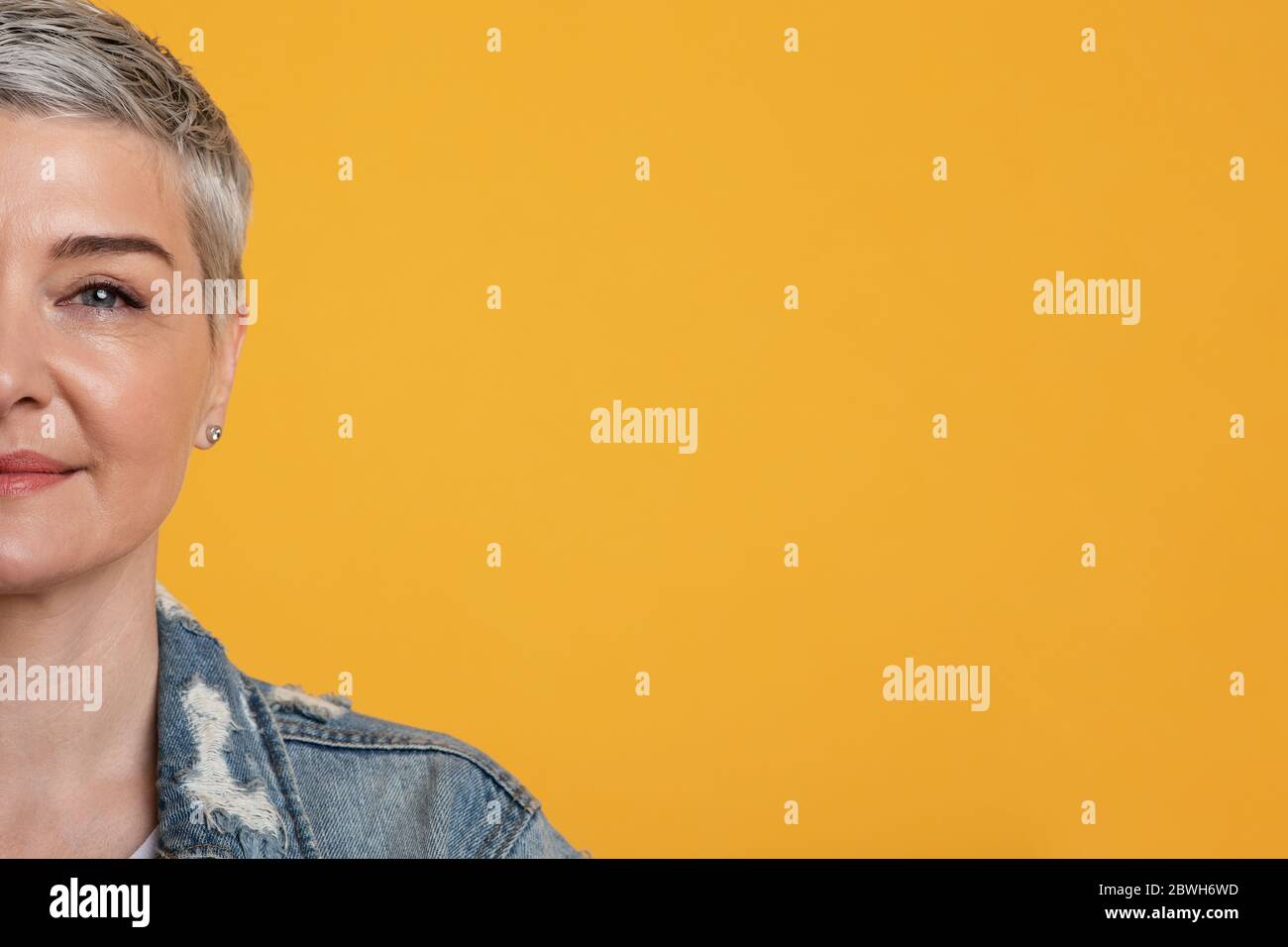 Portrait à demi-visage de la belle femme d'âge moyen sur fond jaune de studio Banque D'Images