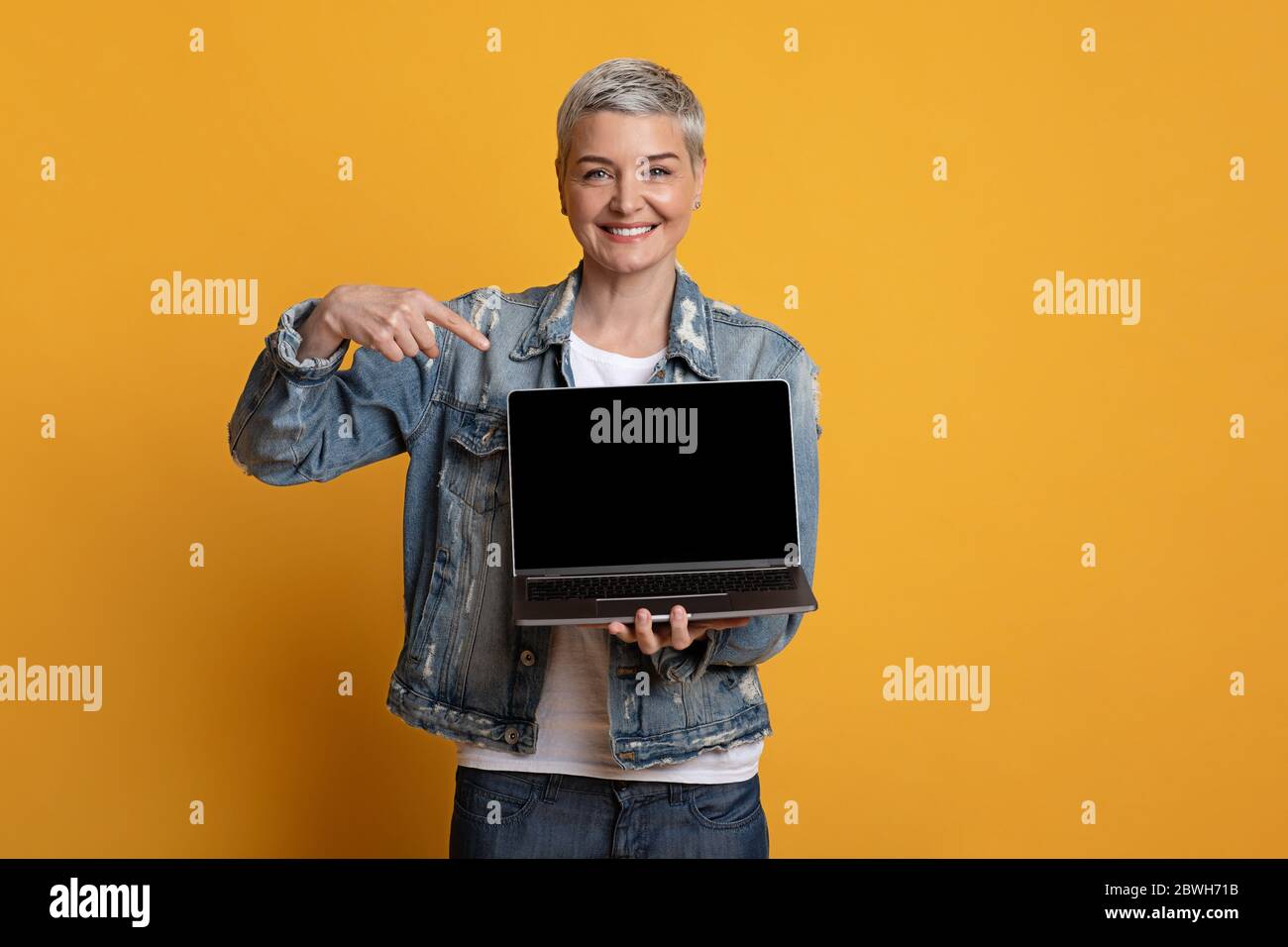 Sites Web indépendants. Femme d'âge moyen positive pointant vers un ordinateur portable avec écran noir Banque D'Images