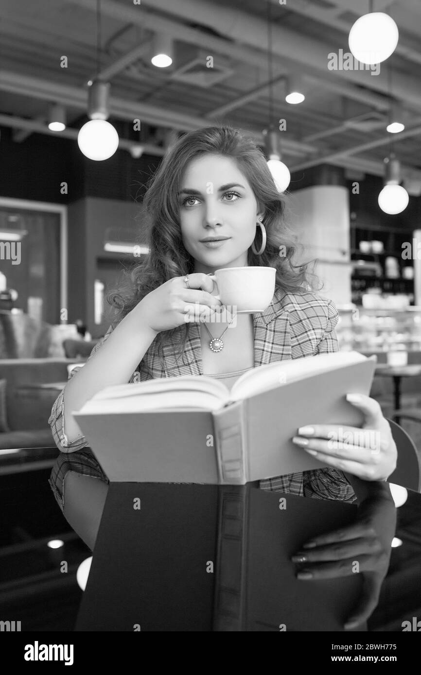 Portrait de jeune belle femme boit le café et livre de lecture dans l'intérieur du café Banque D'Images
