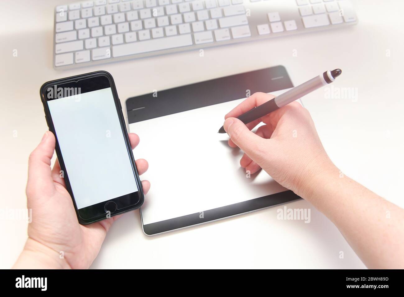 Station de travail minimaliste avec mains tenant une tablette à stylet et un smartphone. Banque D'Images