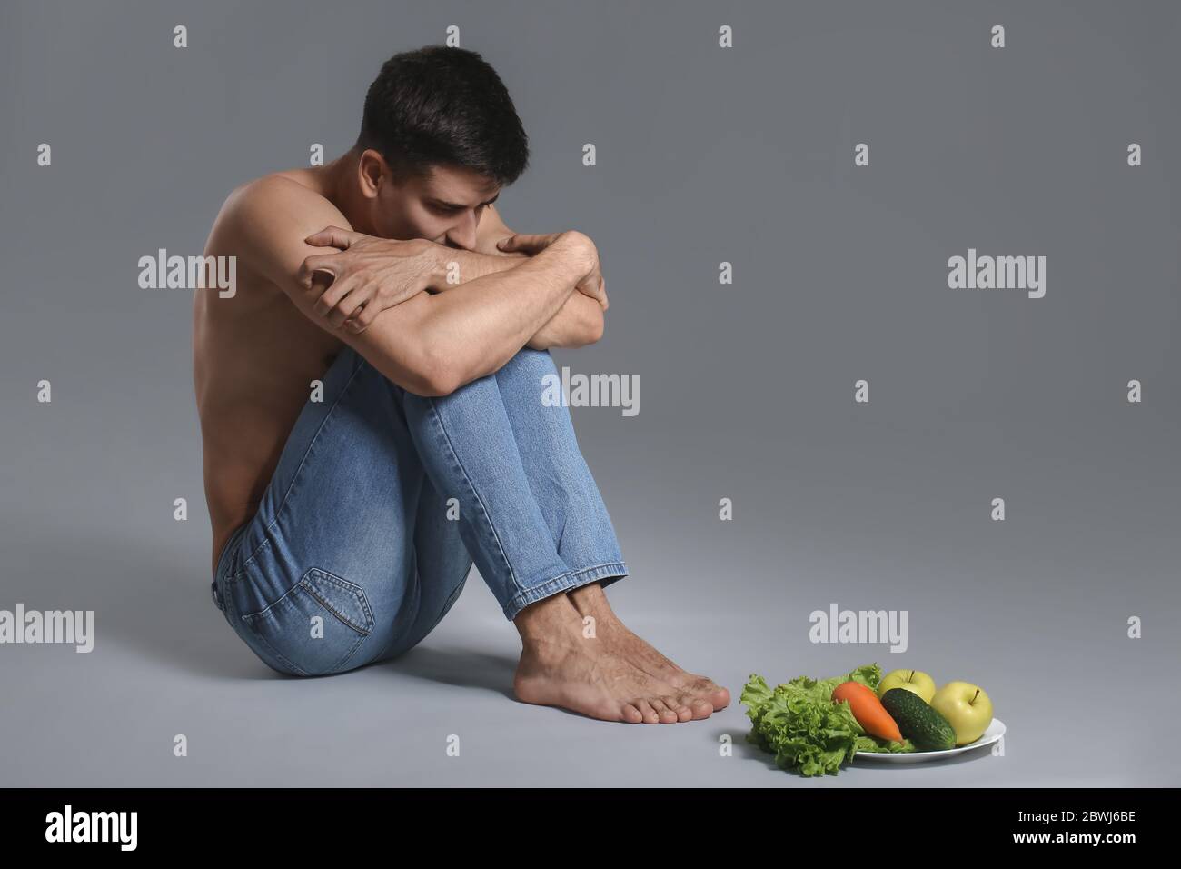 Homme malade avec des légumes frais sur fond gris. Concept d'anorexie Banque D'Images