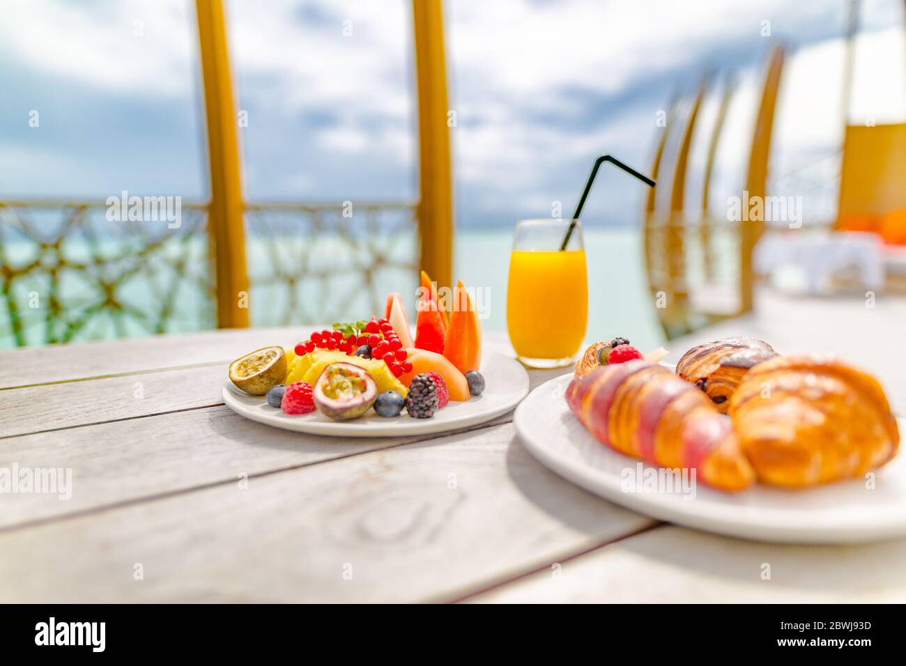 Petit-déjeuner avec croissants, jus d'orange et fruits. Table du matin du complexe tropical avec vue floue sur la mer. Banque D'Images