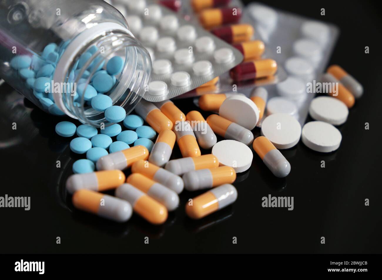 Pilules sur une table en verre foncé, différents médicaments en capsules et comprimés dispersés d'une bouteille. Concept de pharmacie, antibiotiques, vitamines Banque D'Images
