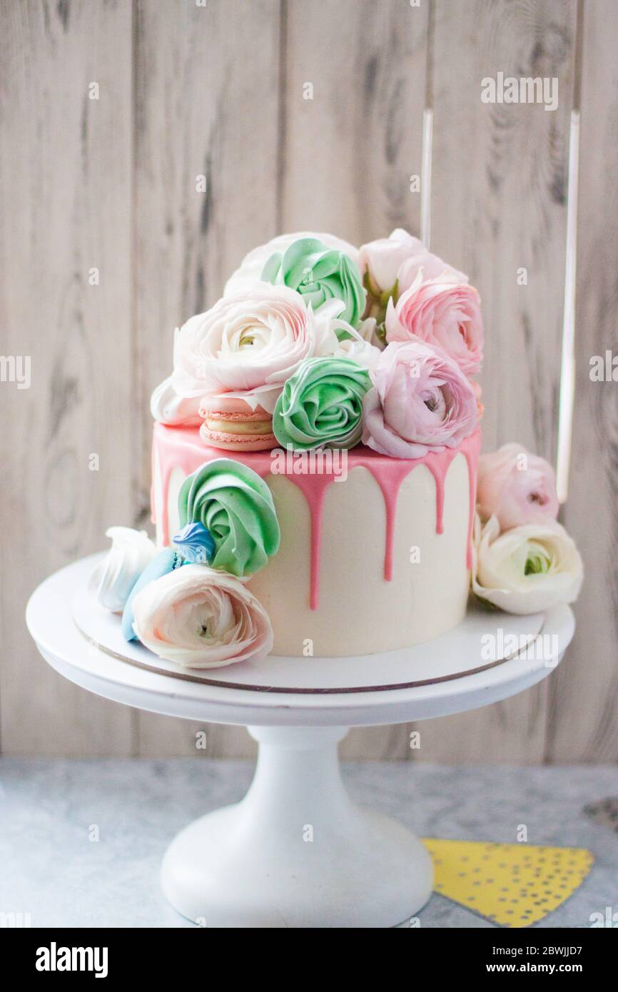 Gâteau blanc au chocolat fondu rose, meringues, macarons et fleurs fraîches. Arrière-plan rustique. Banque D'Images
