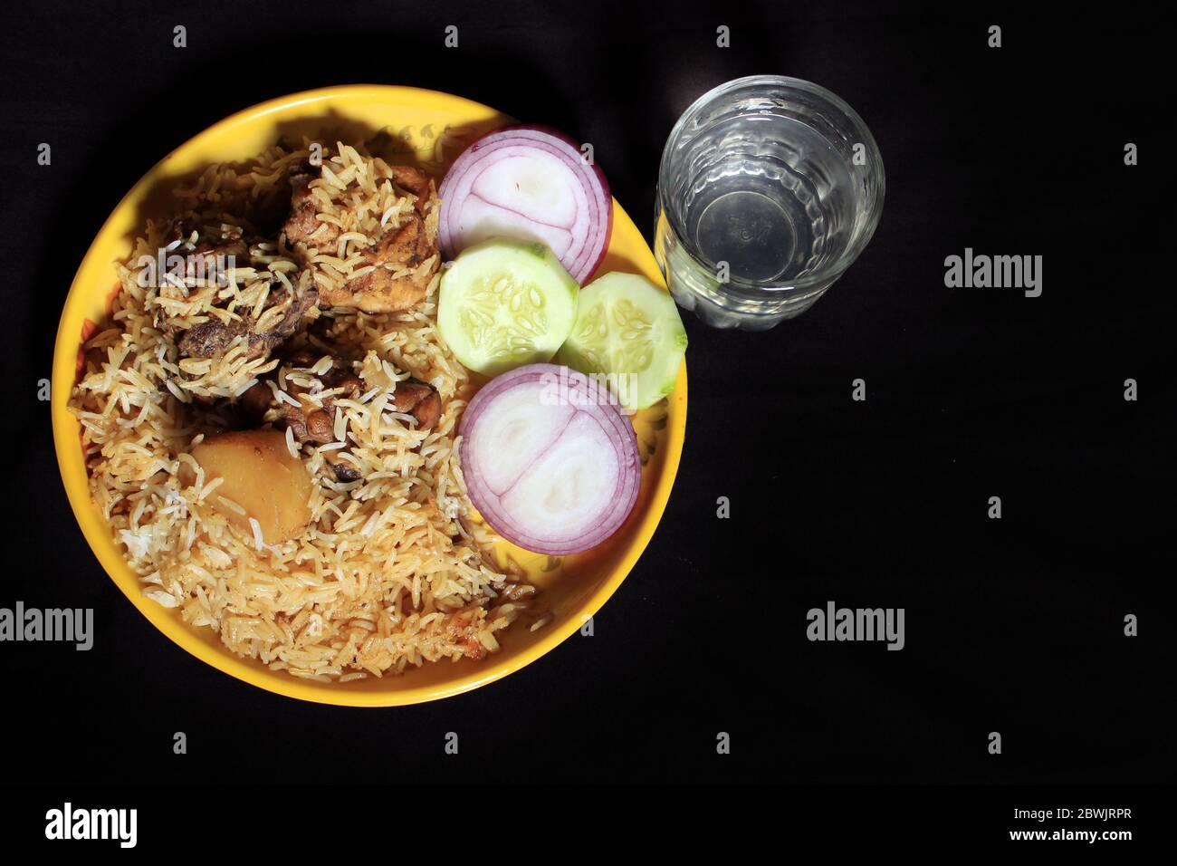 Délicieux poulet indien délicieux Biriyani sur une plaque jaune isolée sur fond noir. Poulet indien Biriyani Curry Food avec concombre et oignon. Banque D'Images
