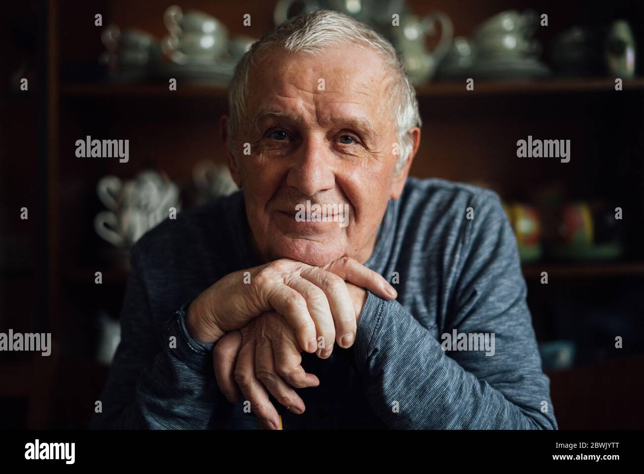 Homme âgé avec bâton de marche assis à la maison. Portrait de l'homme âgé dans les années 80. Banque D'Images