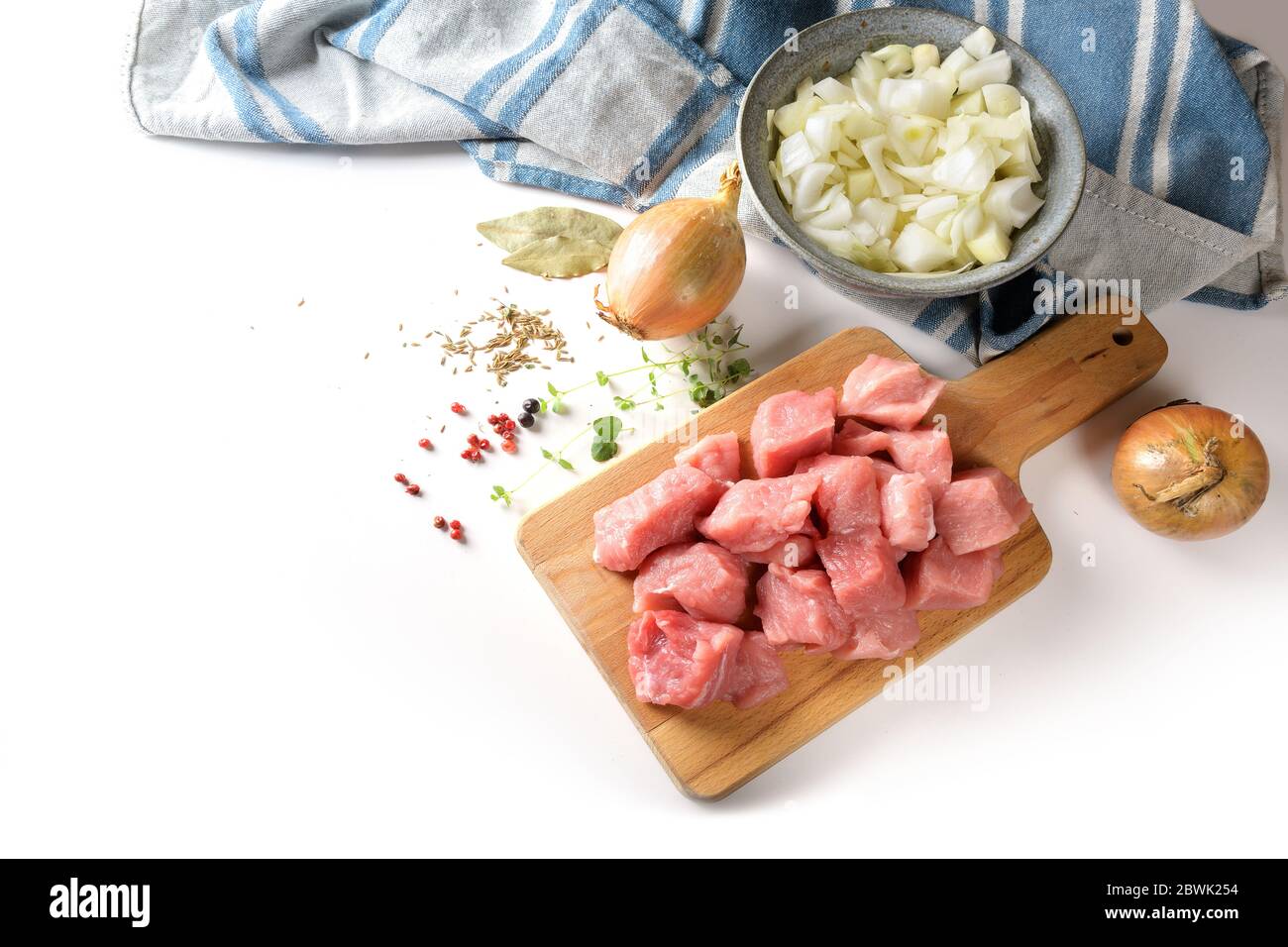 Morceaux de viande de porc crus, oignons, herbes et épices, ingrédients de cuisine pour un ragoût savoureux, goulash ou ragoût, sur un plan de cuisine, isolé sur une cose blanche Banque D'Images