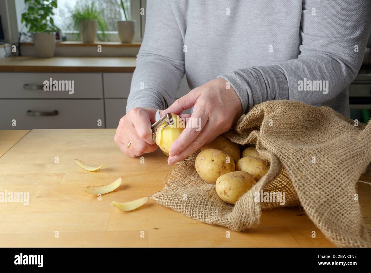 Les mains d'une femme éplucher des pommes de terre crues sur une table en bois dans la cuisine à la maison, foyer choisi, profondeur de champ étroite Banque D'Images