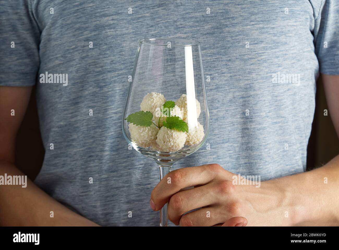 Truffes à la noix de coco blanche dans un verre à vin avec congé à la menthe. Homme tenant un verre de vin avec des biscuits à la noix de coco. Banque D'Images