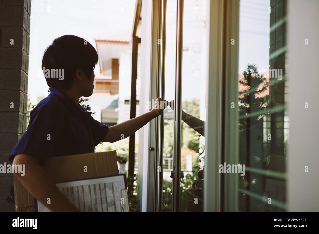 Le jeune messager asiatique utilise la main du coup à la porte pour livrer les marchandises. Banque D'Images