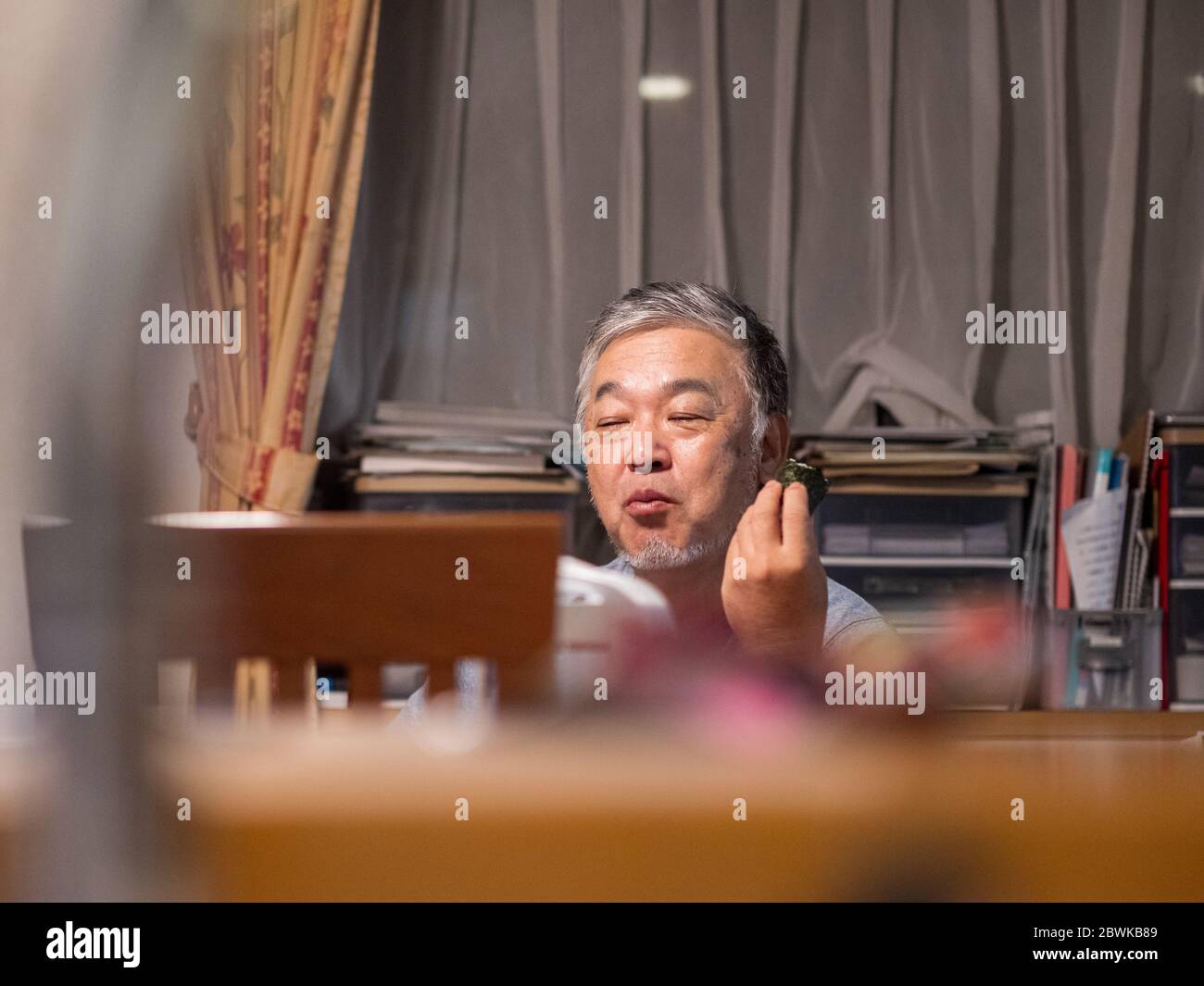 Un homme plus âgé qui apprécie une boule de riz 'onigiri' dans sa maison Banque D'Images